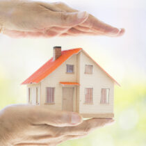 Female hands holding and saving small wooden house. Household concept.