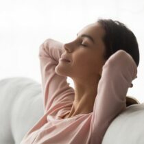Side close up view serene young woman holds hands behind head closed eyes feels placidity, tranquil girl having day nap leaning on comfortable sofa in living room, refreshment and daydreaming concept
